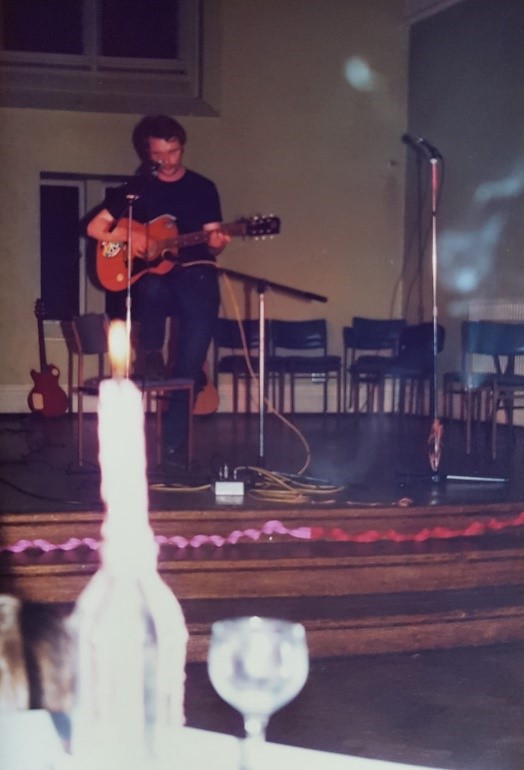 John Carroll playing the guitar on stage at, presumably, the January 1984 religious studies department social.