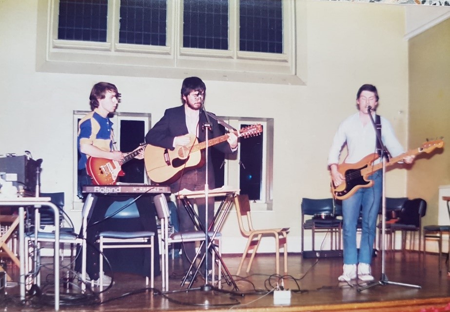 Richard Powell, Peter Brindley, and Sean Delaney playing music on stage at, presumably, the January 1984 religious studies department social.