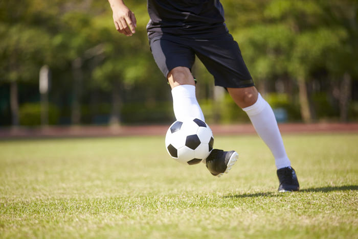 Lower half of footballer bring football under control on grass field