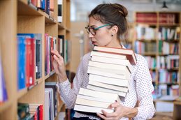 Student carrying a pile of books in the library