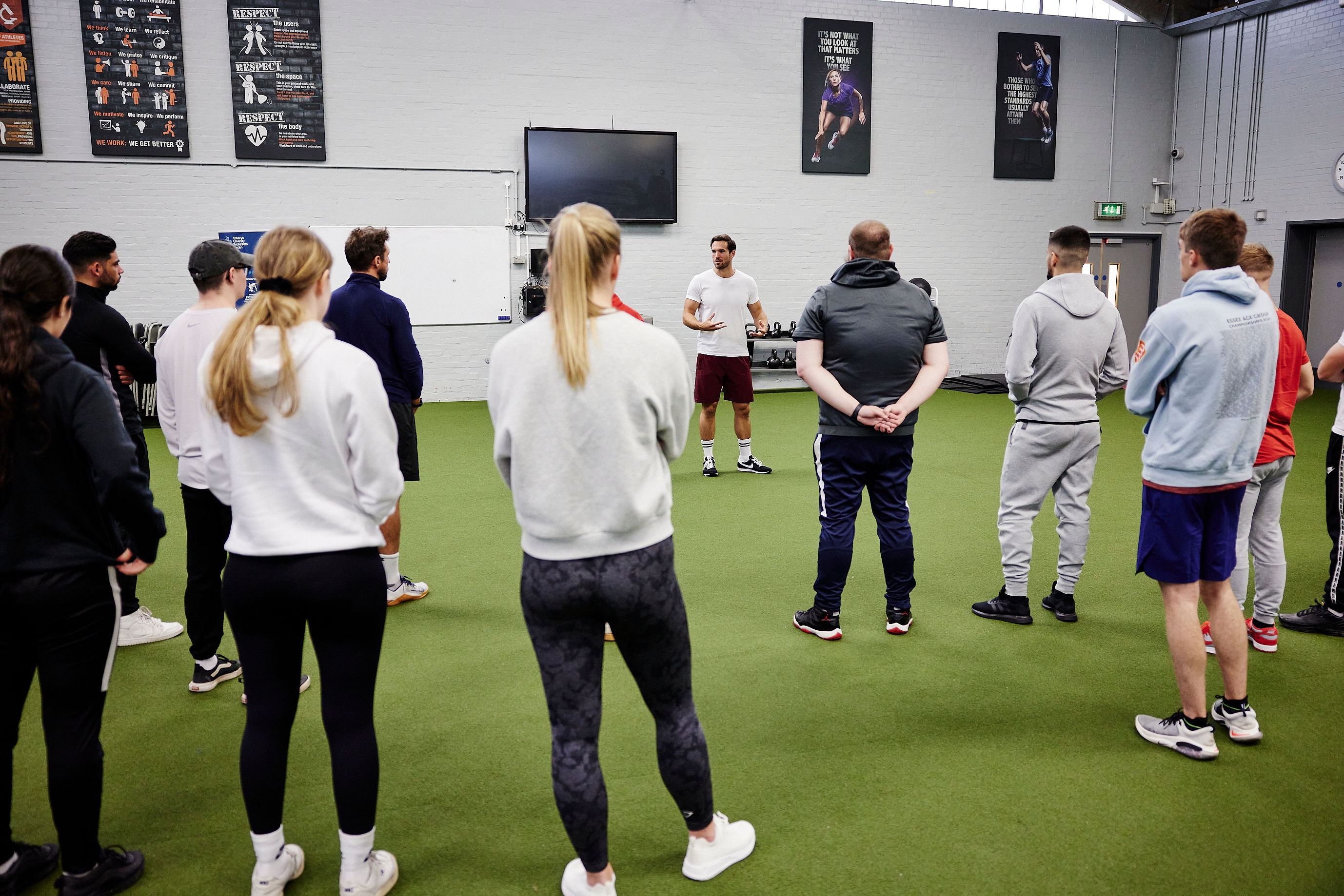 Students stood listening to a lecturer in the PEC.