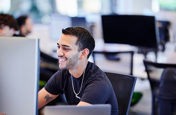 A student sits by a computer in a computing lab.