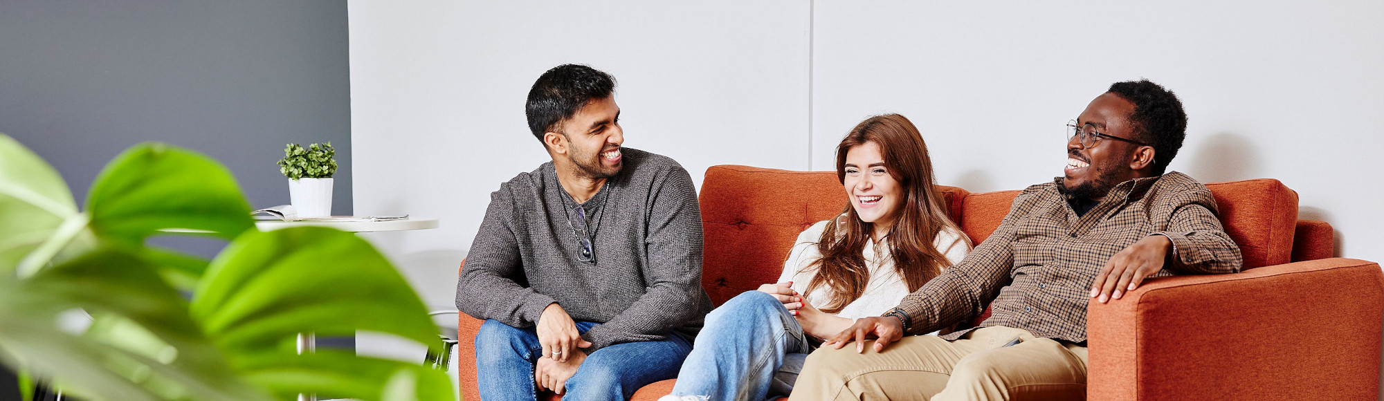Three students sit on a sofa talking to one another.