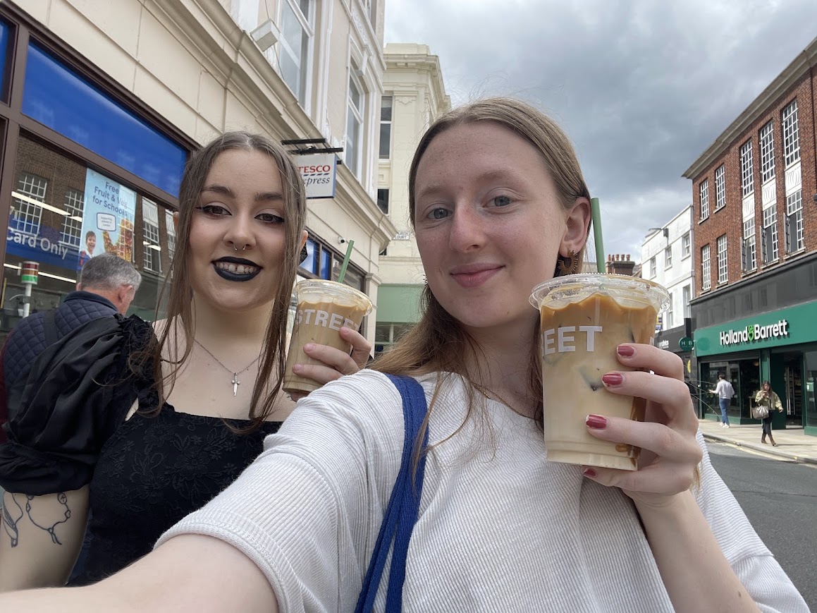 Two students holding iced coffees on a sunny street in the local area near St Mary's University.