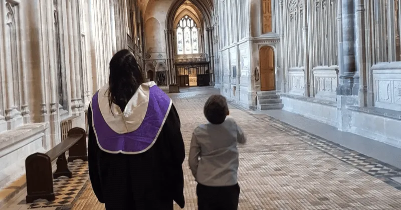 Charley and her son walking inside a large, ornate hall with high vaulted ceilings and stone walls.