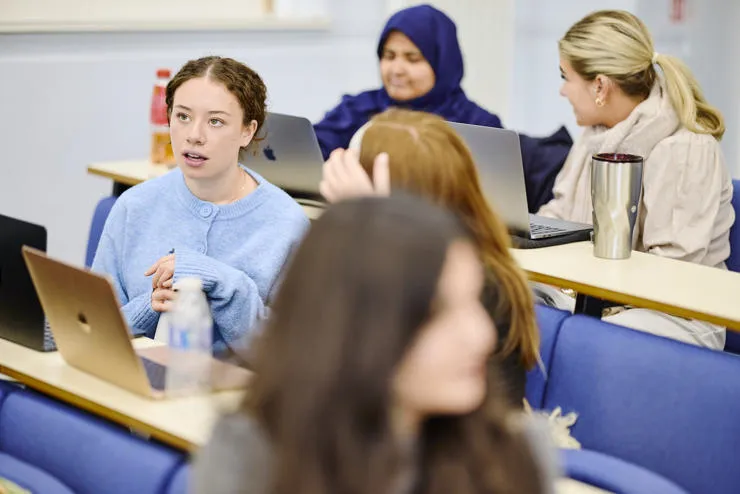 Students sit in front of computers discussing a topic during a tutorial.