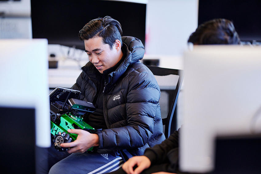 A student sits in a computer lab holding a robotic vehicle during an Artificial Intelligence course at St Mary's University, London.