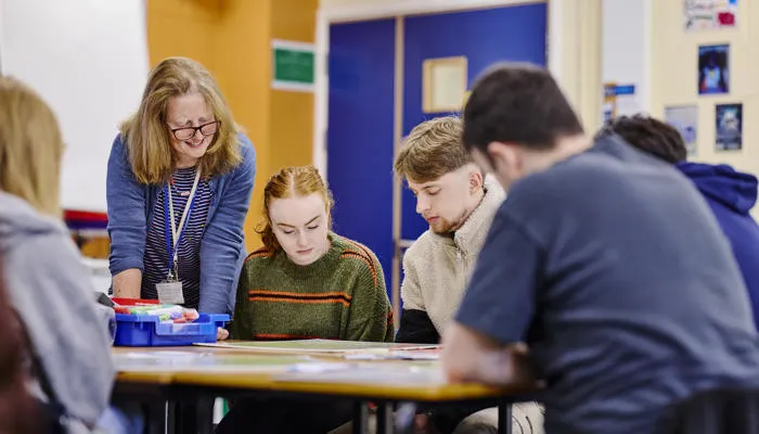 Students sit around a table as their tutor supports their learning.
