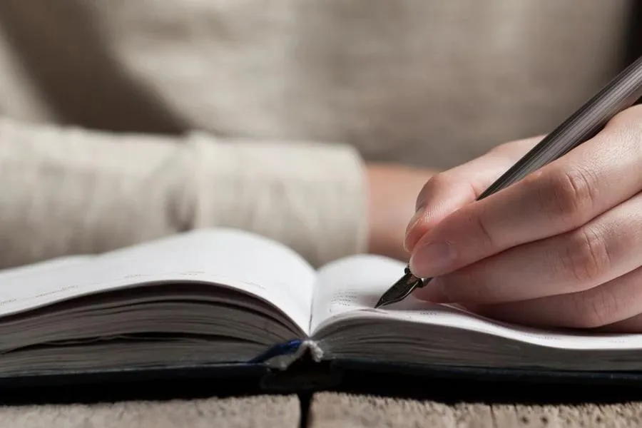 Person writing with a pen in an open notebook.