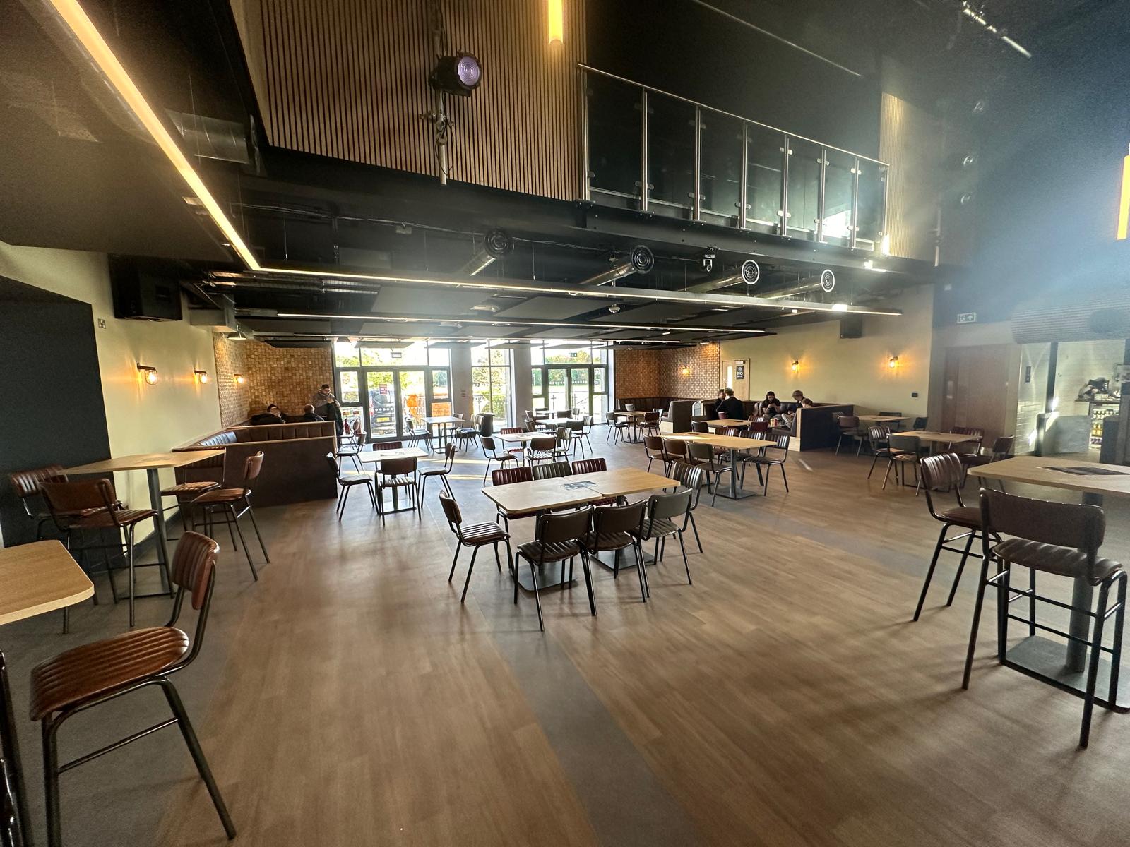 Café-bar interior with wooden tables, leather-style chairs and a mezzanine level.