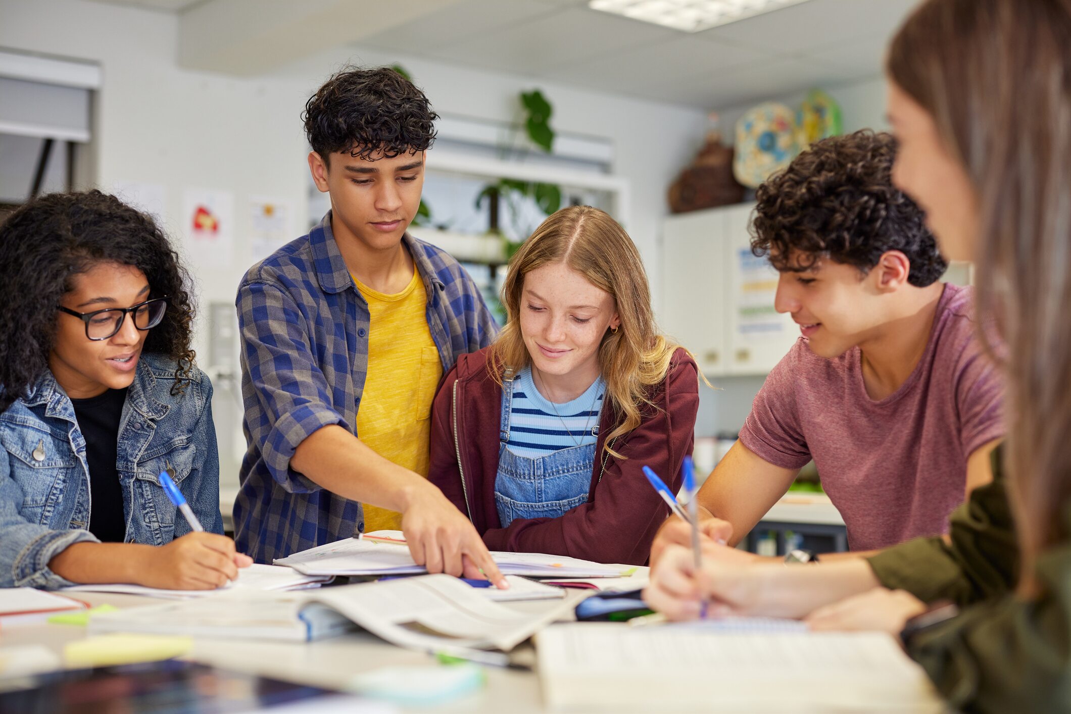 Five students studying together around a table in a classroom.