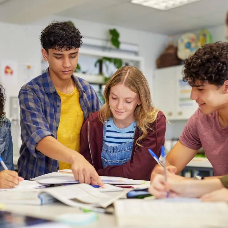 Five students studying together around a table in a classroom.