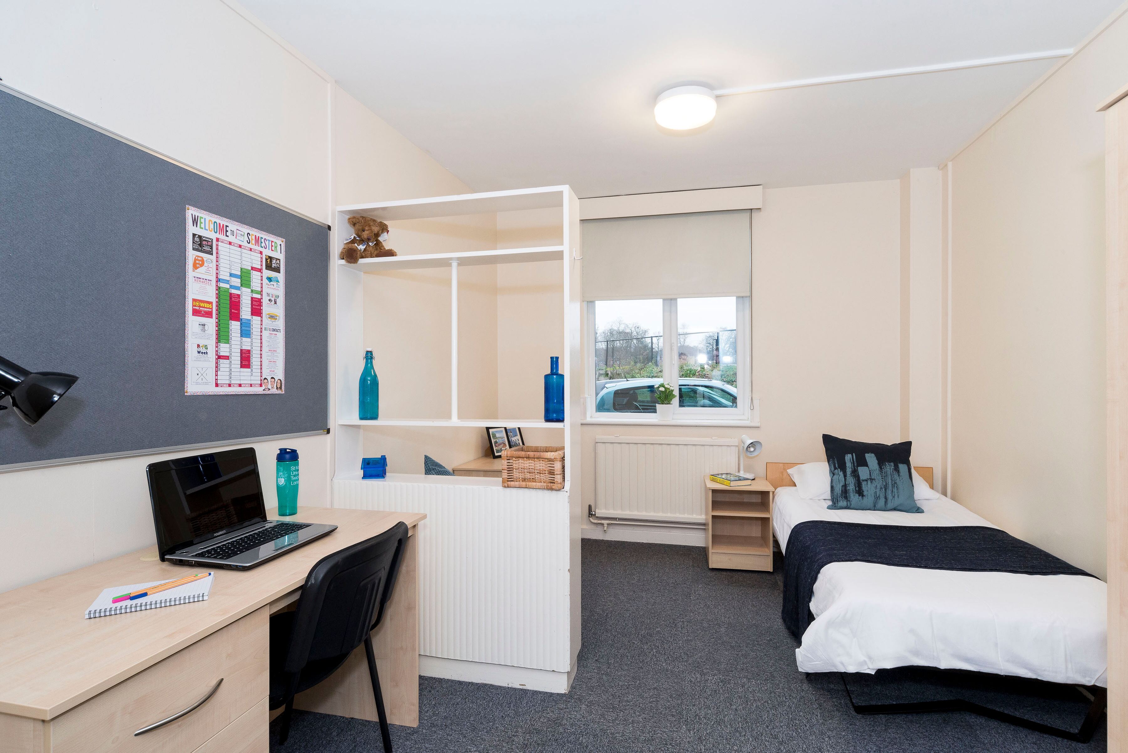 Student bedroom with a single bed, desk and shelving used as a room divider.