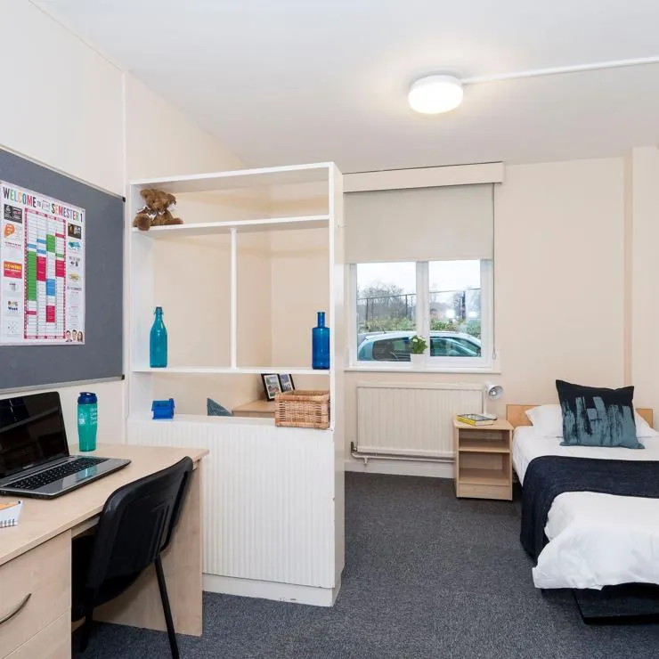 Student bedroom with a single bed, desk and shelving used as a room divider.