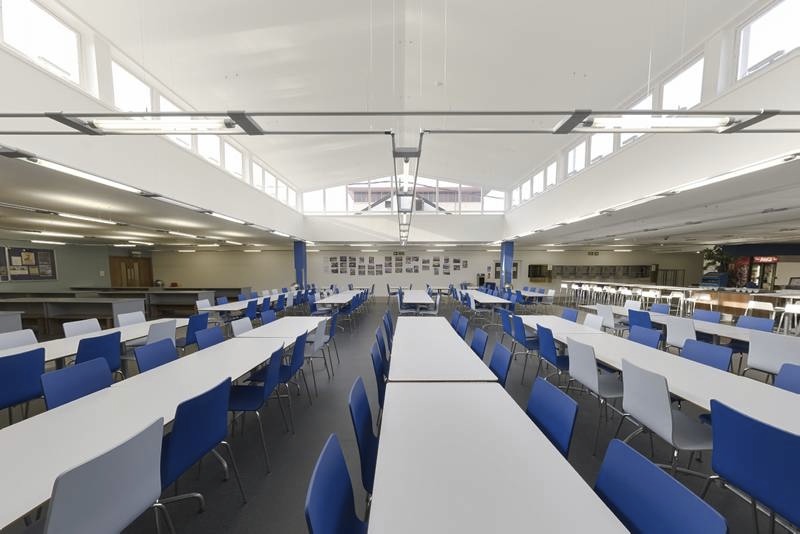 Refectory dining hall with long white tables and blue and grey chairs.