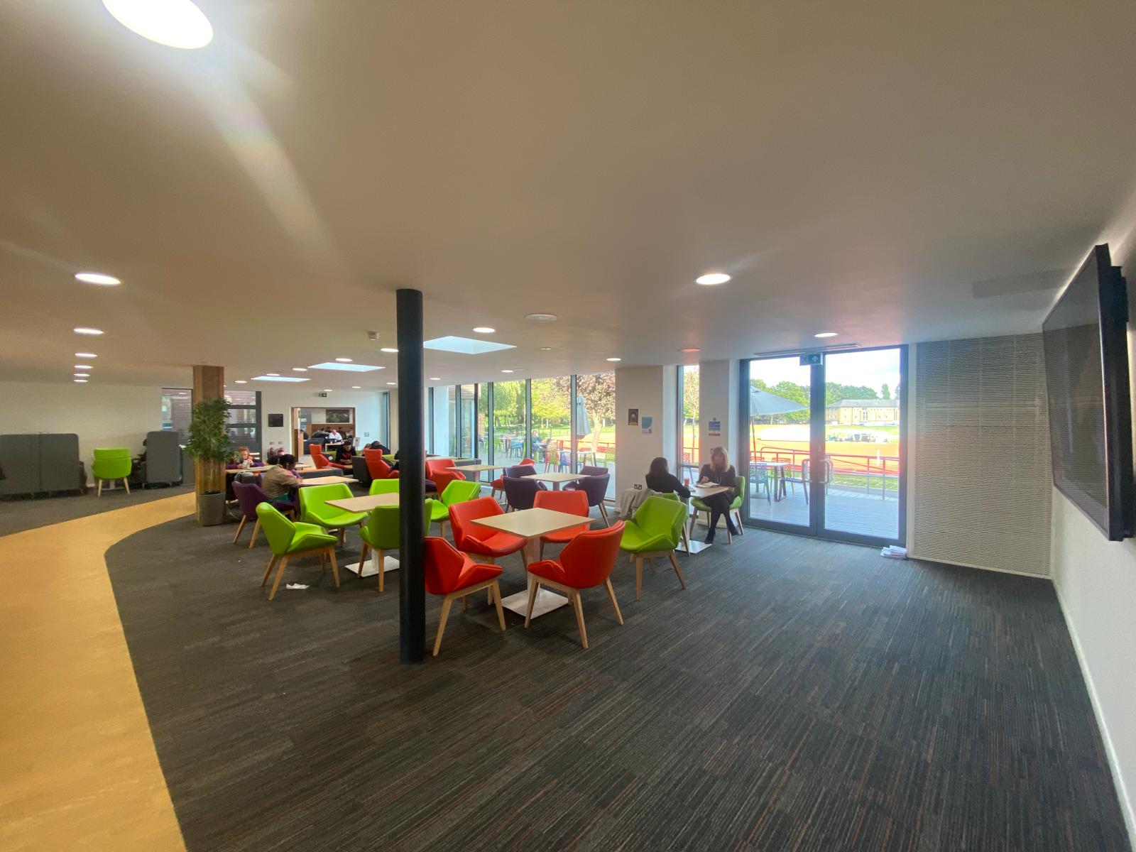 Social space with tables and colourful armchairs beside large windows.