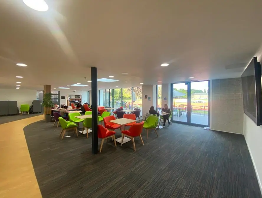 Social space with tables and colourful armchairs beside large windows.