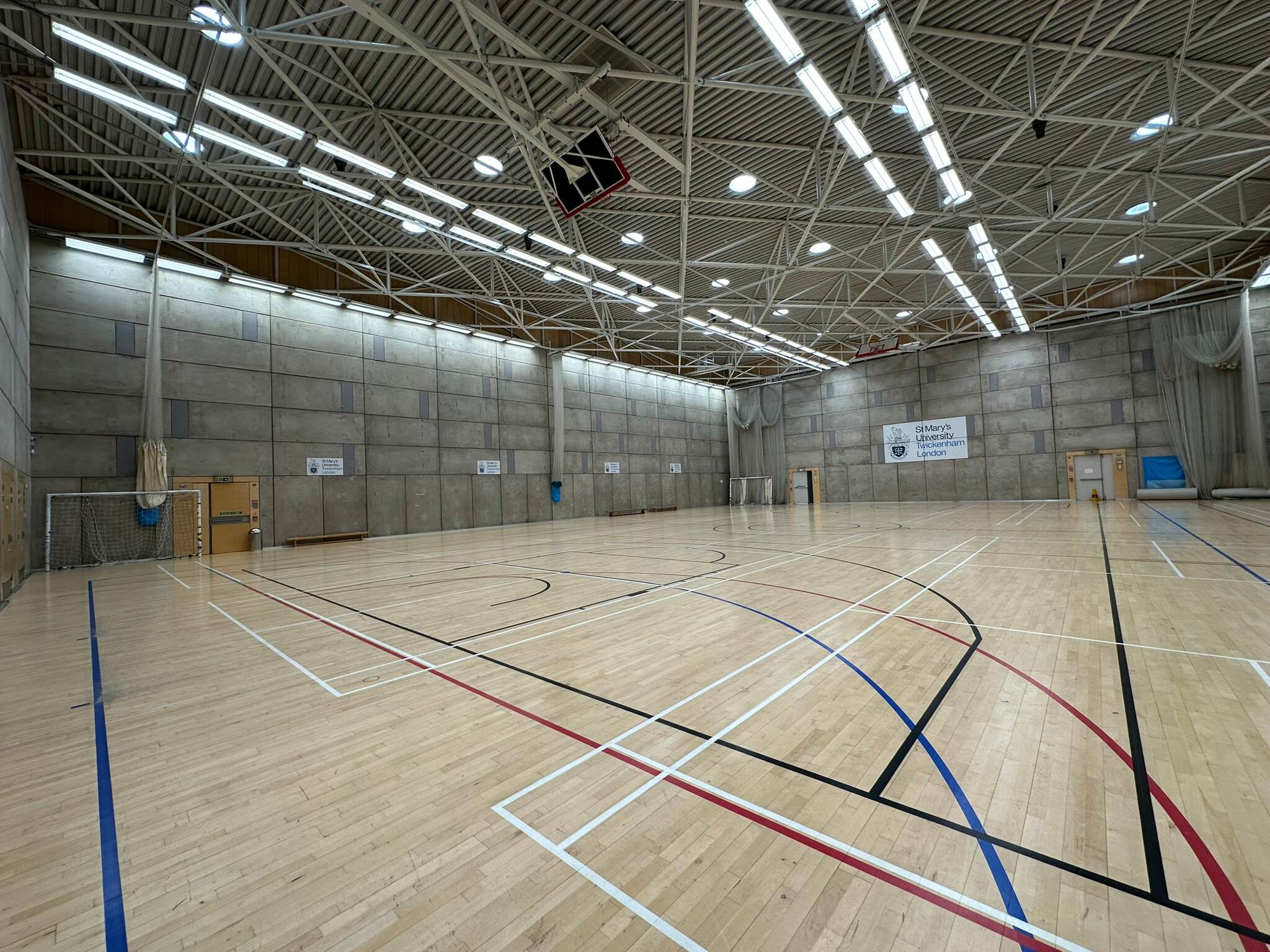 Indoor sports hall with a wooden floor, basketball hoops and a St Mary's banner.