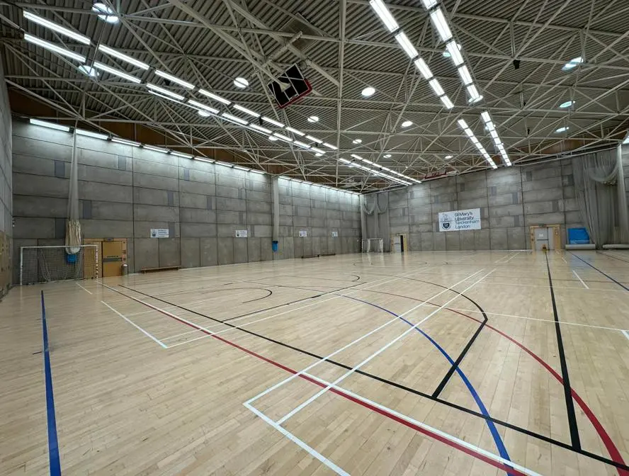 Indoor sports hall with a wooden floor, basketball hoops and a St Mary's banner.