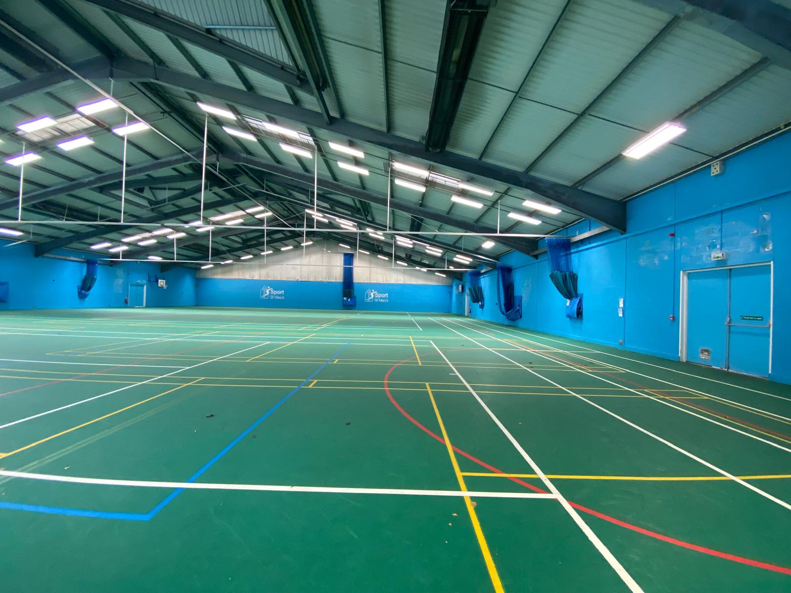 Large indoor sports hall with a green multi-court surface and blue walls.
