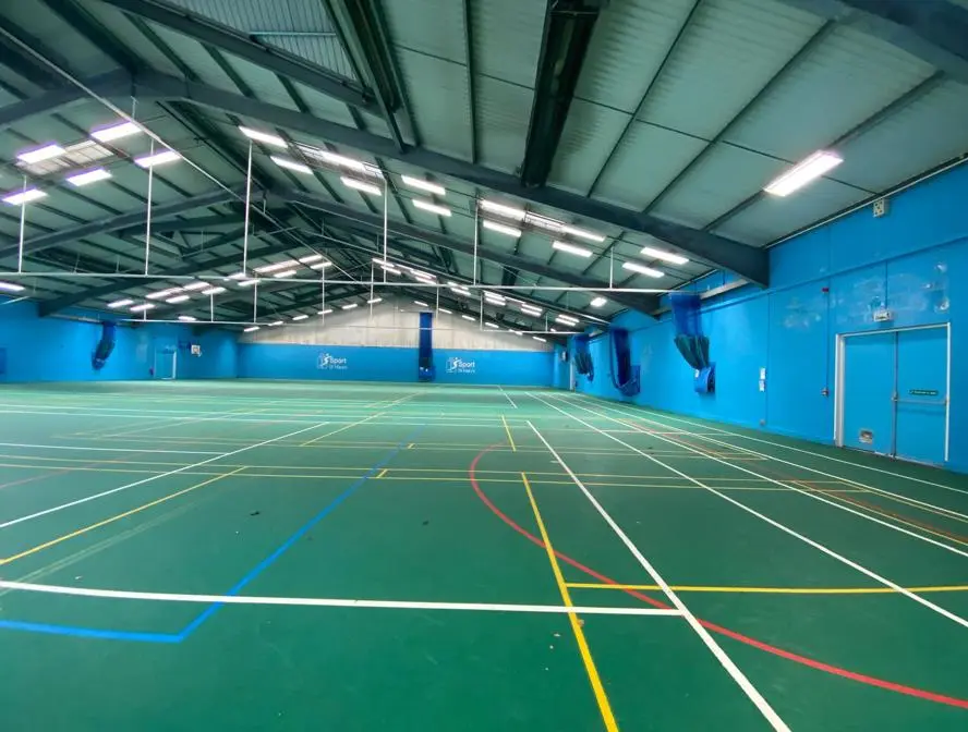 Large indoor sports hall with a green multi-court surface and blue walls.