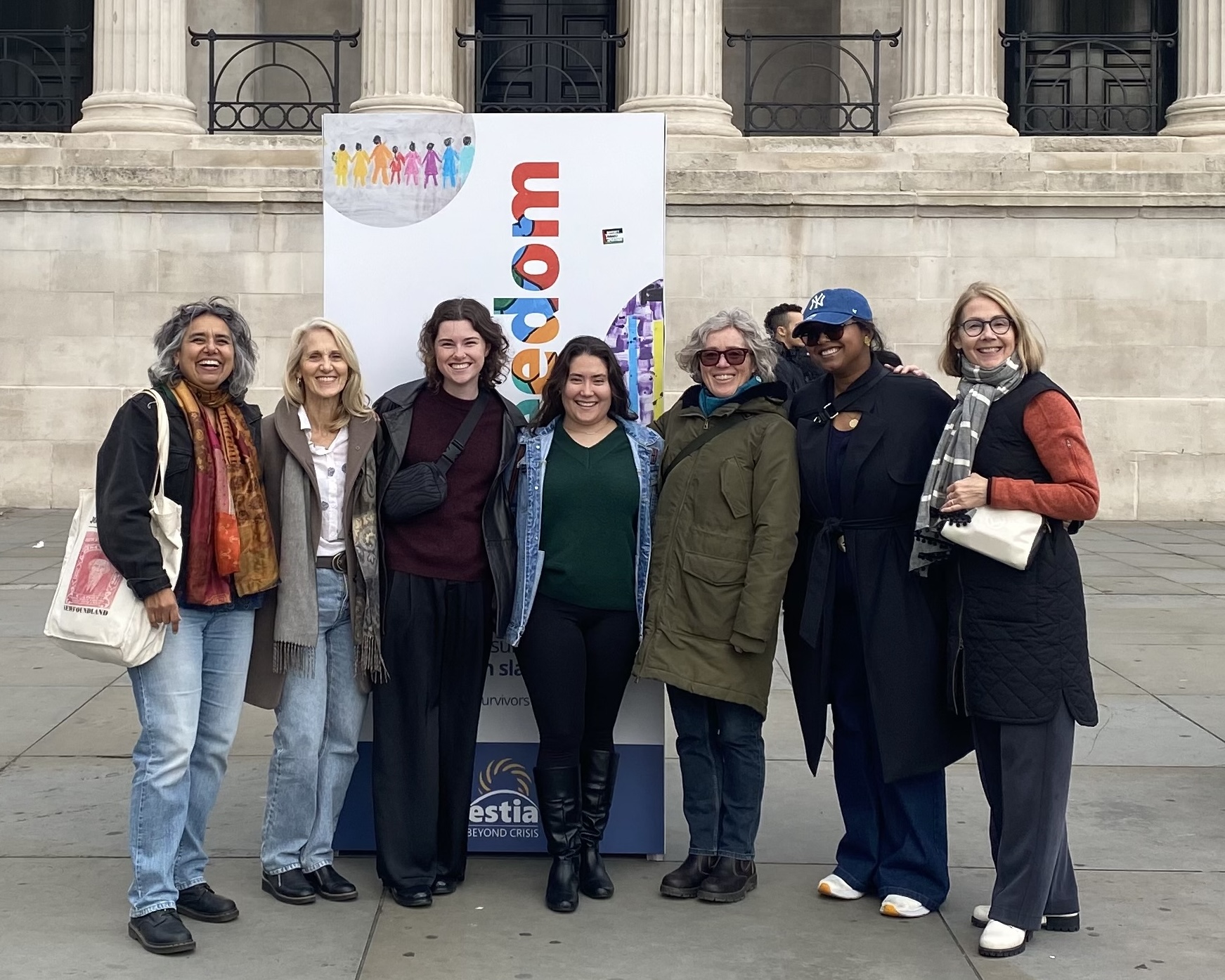 A group of master's students pose in front of a sign with teaching staff while attending an event.