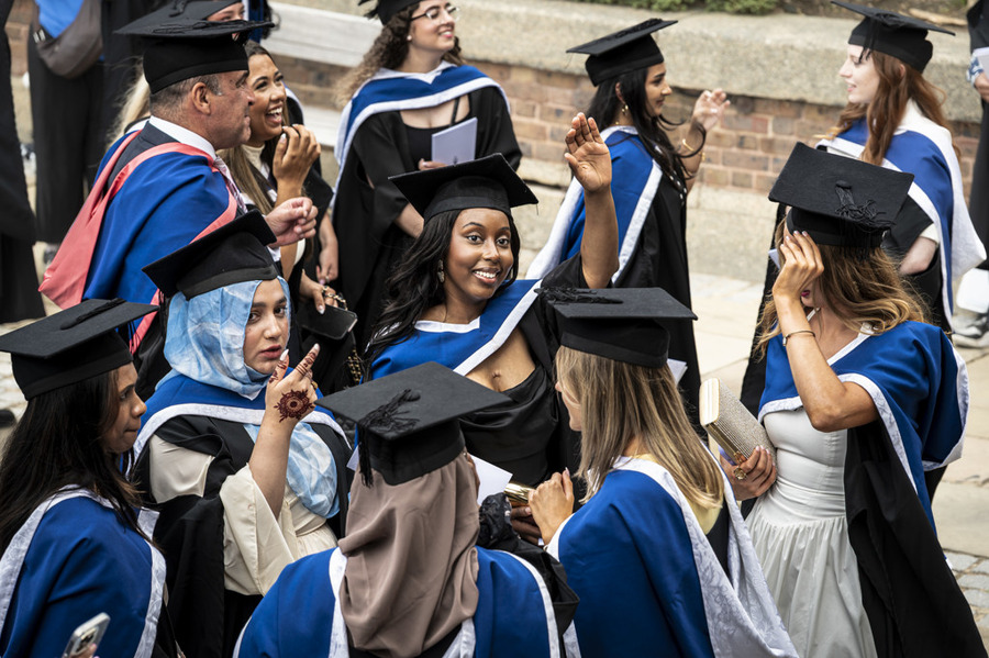 Graduates in caps and gowns gather outdoors, smiling and celebrating together.