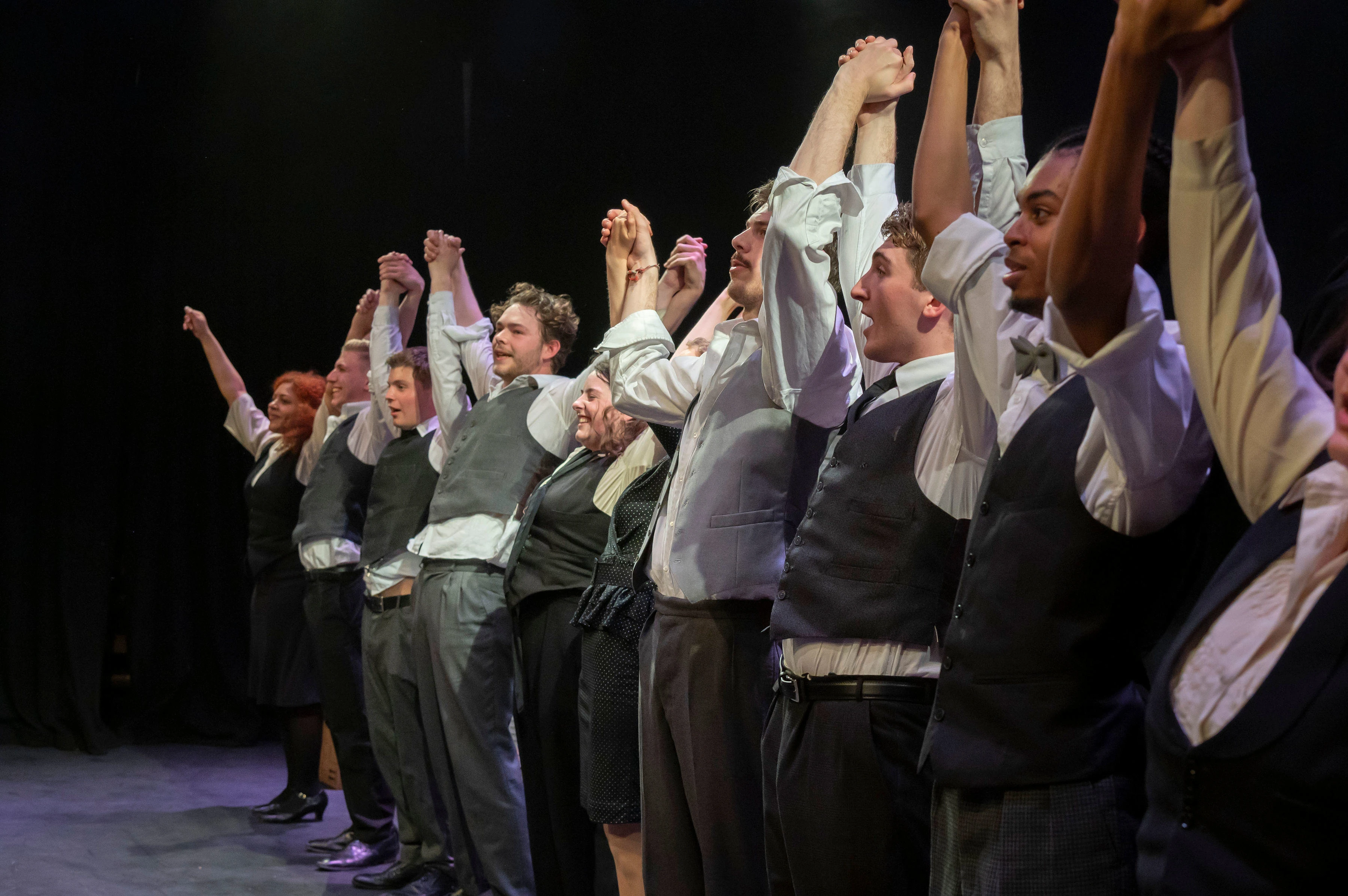 Performers on stage holding hands and raising their arms together, appearing to take a bow at the end of a show.