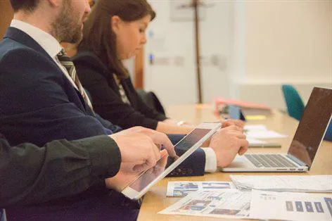 Business students sat at a desk using a laptop and ipad.