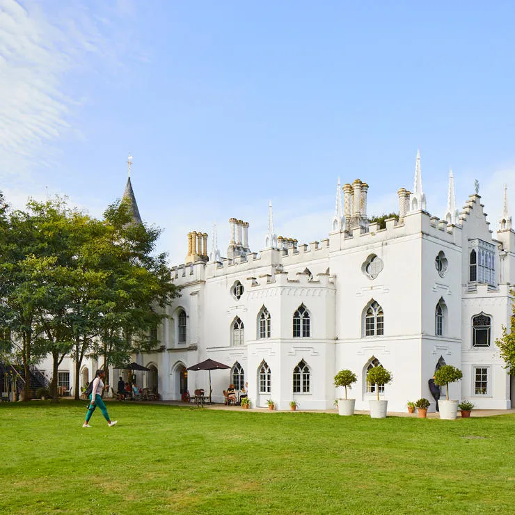 A student walking past Strawberry Hill House surrounded by greenery.