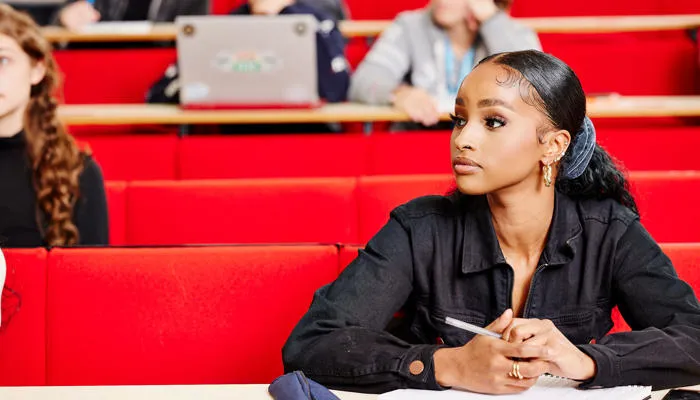 A student sits in a lecture theatre. The seats are bright red.
