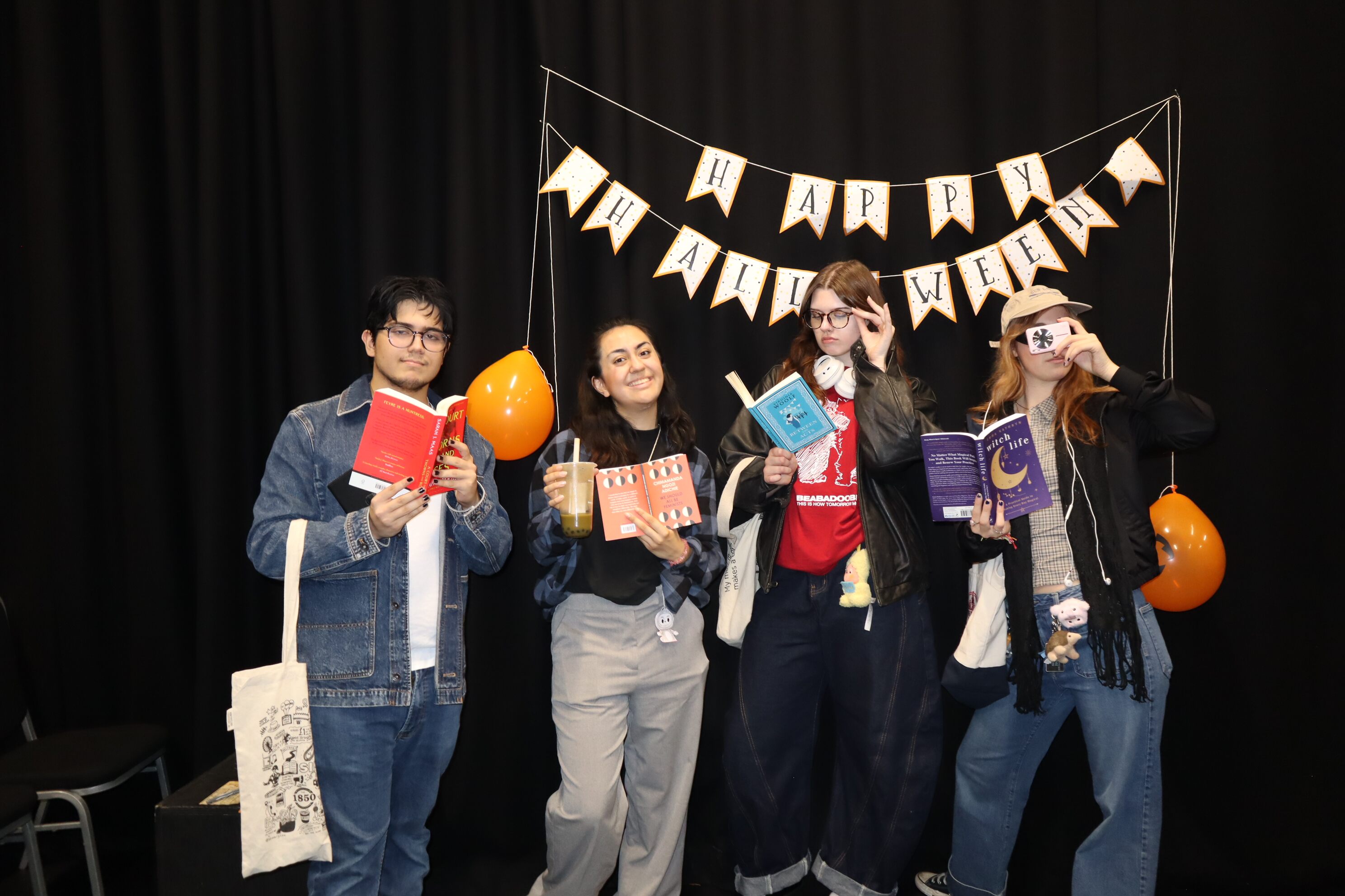 Four St Mary's students holding books in front of a Happy Halloween sign.