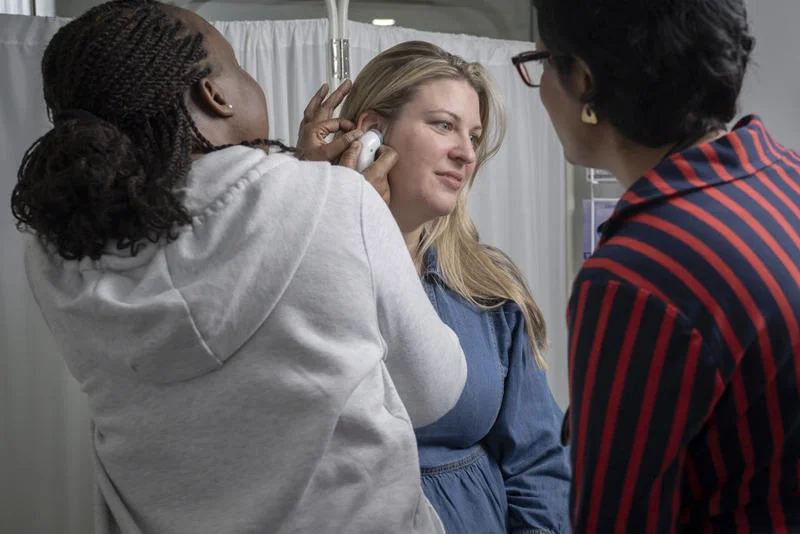 A woman receives a medical examination from a trainee doctor while another observes closely.