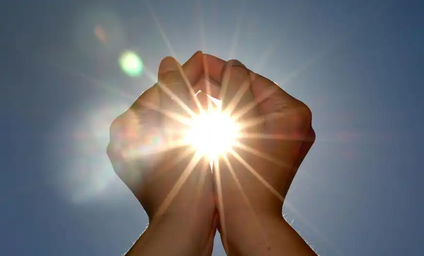 Two hands held up to the sky as the sun shines through, creating a star shape.