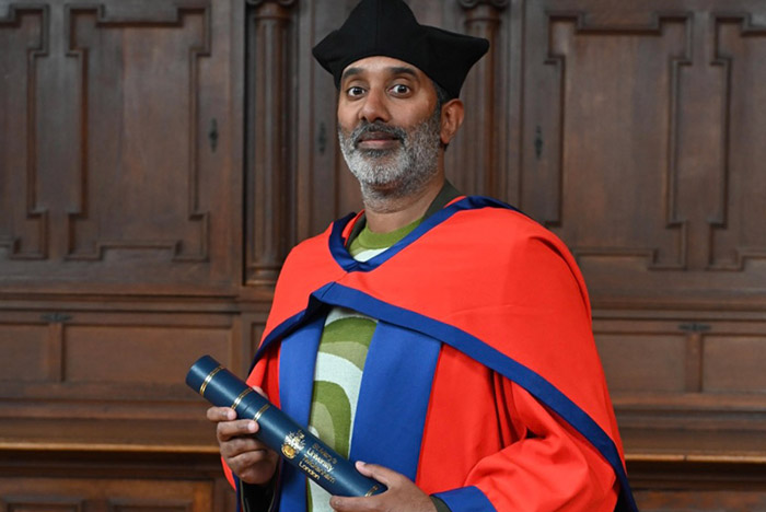 Nihal Arthanayake in red doctorate robe holding degree certificate in tube