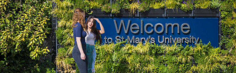Students walking by the welcome sign to the university.