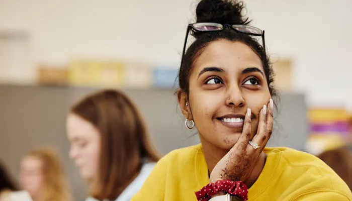 A student in a yellow sweatshirt and mehndi looks up and smiles in class.