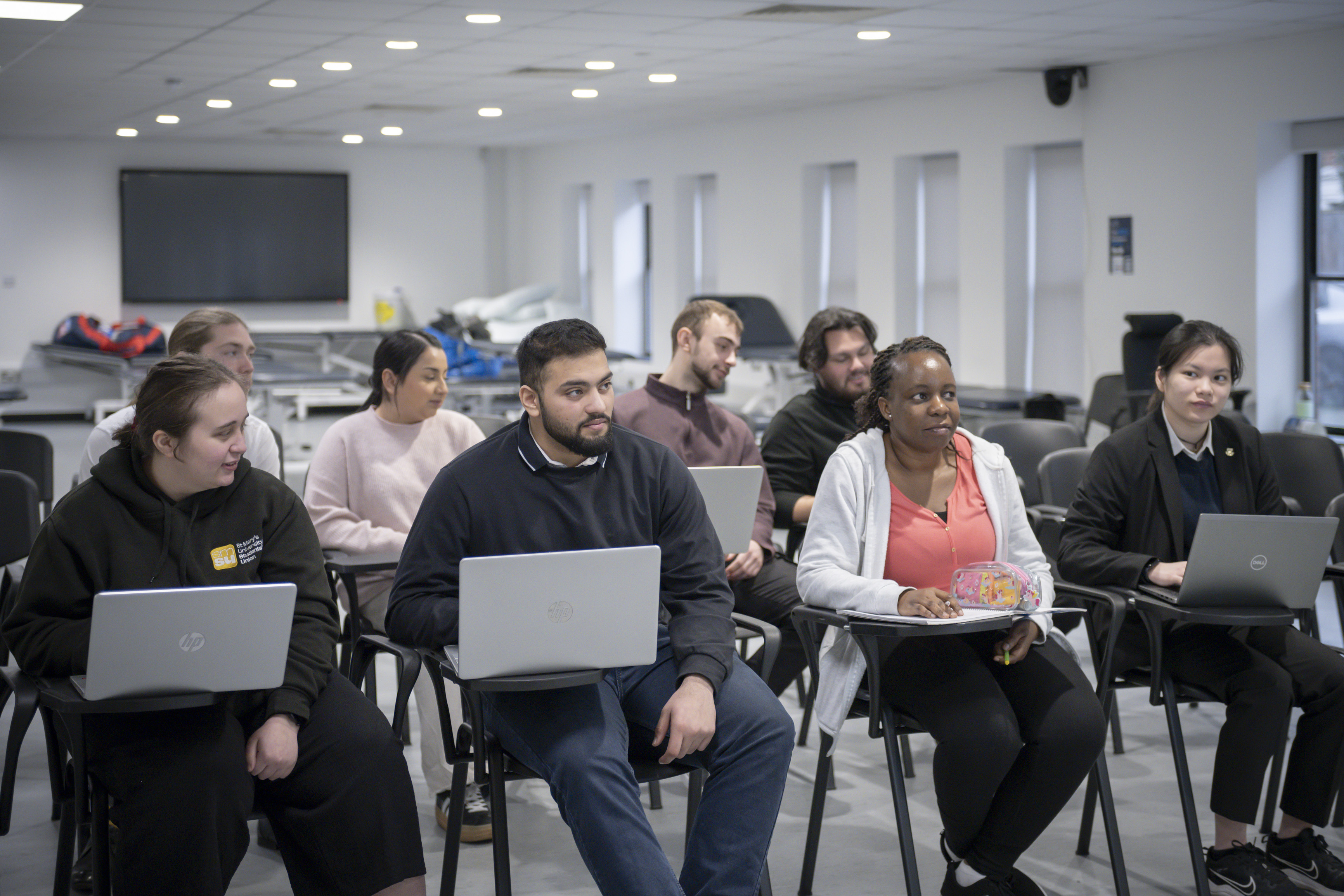 A group of people sit in a classroom, each with a laptop, appearing engaged in a learning session.