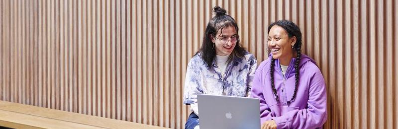 Friends sit and laugh in front of a laptop.
