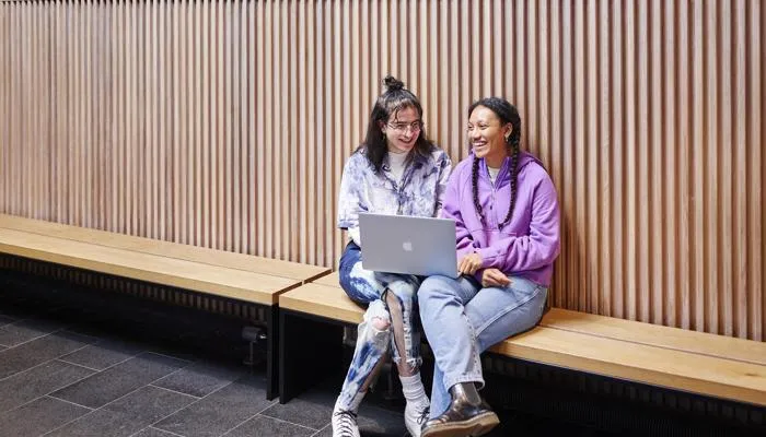 Friends sit and laugh in front of a laptop.