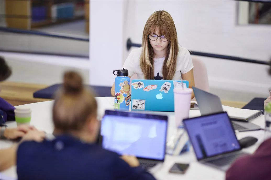 Students sit in a circle on their laptops.
