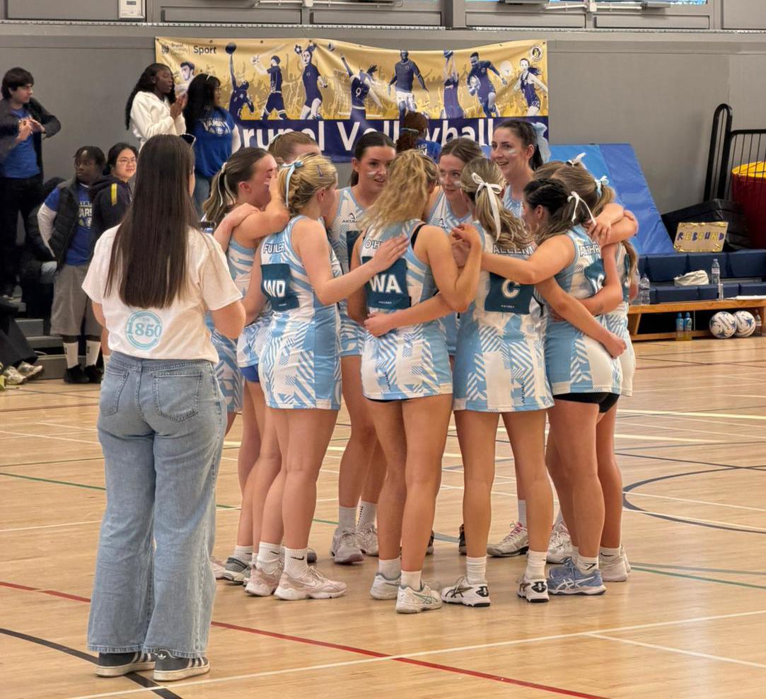The St Mary's University netball team stand in a huddle during a game.