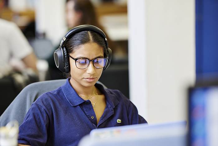 female student with headphones on using laptop in library