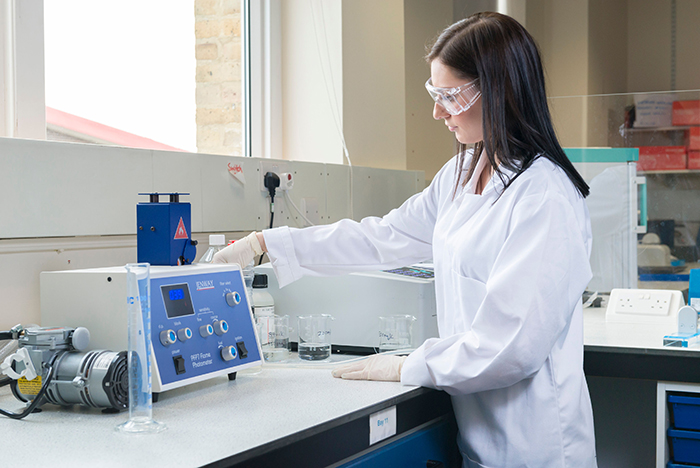 female researcher in white lab coat and personal protective equiptment using lab equiptment. 