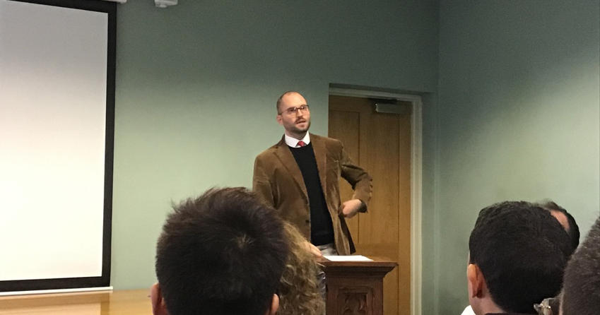 Man delivering lecture from lectern at front of room