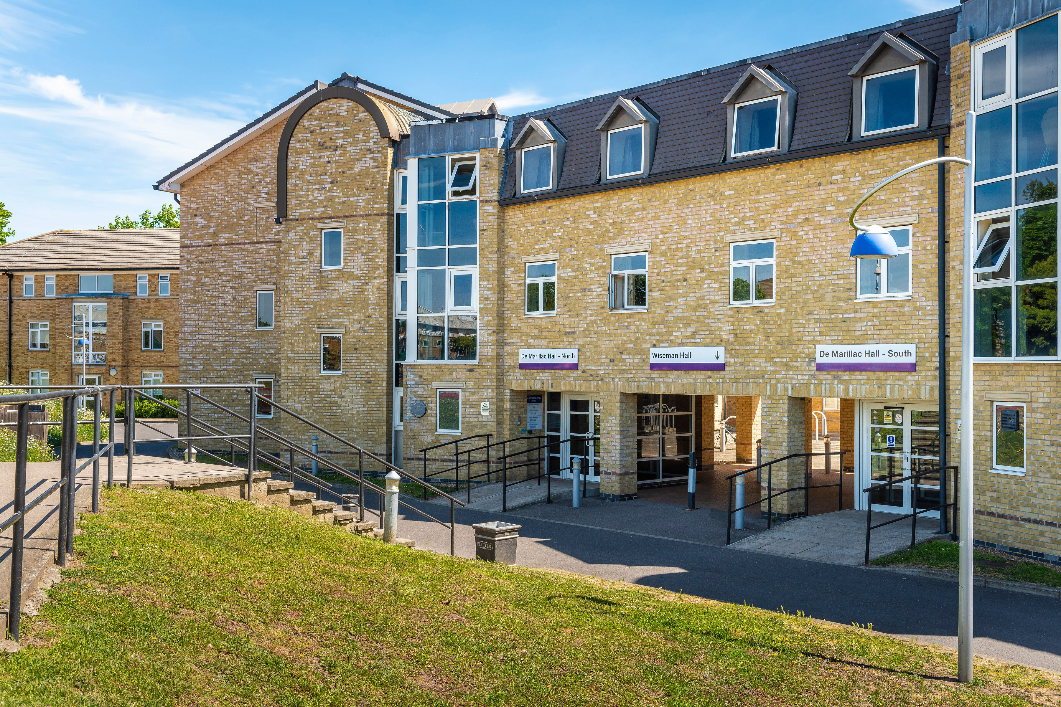 Modern three-story building with large windows, stone exterior, and a grassy area in front under a blue sky.